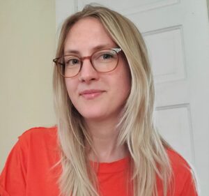 headshot of a young blonde woman with glasses and an orange sweater