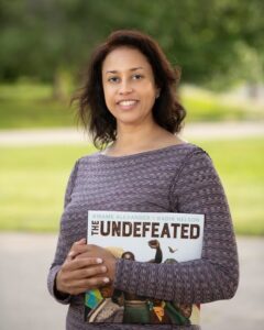 Dr. Krista Aronson holding a book called "The Undefeatd" while standing outdoors