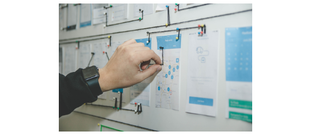 A person creating a physical chart on a pinboard with paper, string, and pushpins