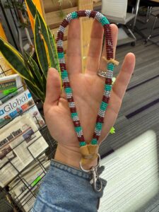 beaded wristlet for keys made by students in white, silver, maroon & teal; its end is wrapped in buckskin.