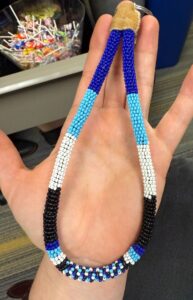 beaded wristlet for keys made by students in red, dark blue, light blue, black; its end is wrapped in buckskin.