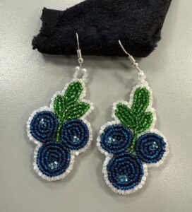 dangly earrings in the shape of three blue blueberries with green vegetation and outline in white beads.